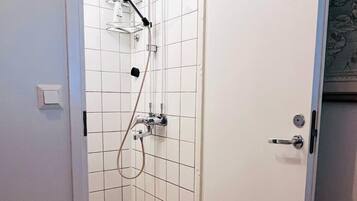 A bathroom with white tiled walls, a shower with a handheld showerhead, and a door with a handle.