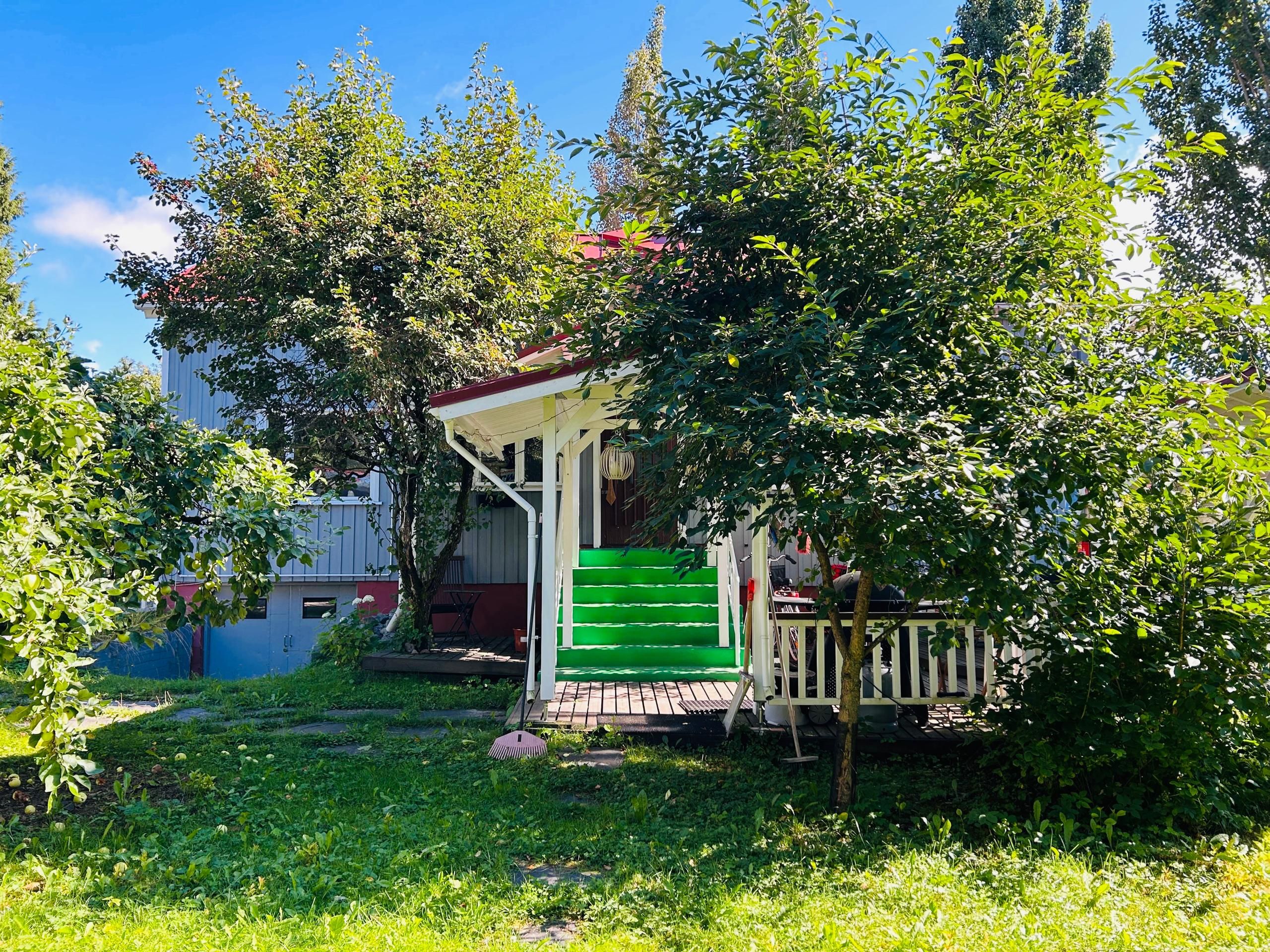Ett litet hus med en grön ytterdörr, en veranda och en trappa som leder upp till entrén.
