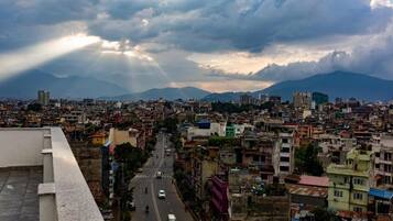 Un paisaje urbano con vistas a montañas distantes, una calle concurrida y edificios de diferentes alturas.