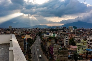 A cityscape with a view of mountains in the distance, a busy street, and buildings of various heights. - Bardan Boutique Hotel (Kathmandu)