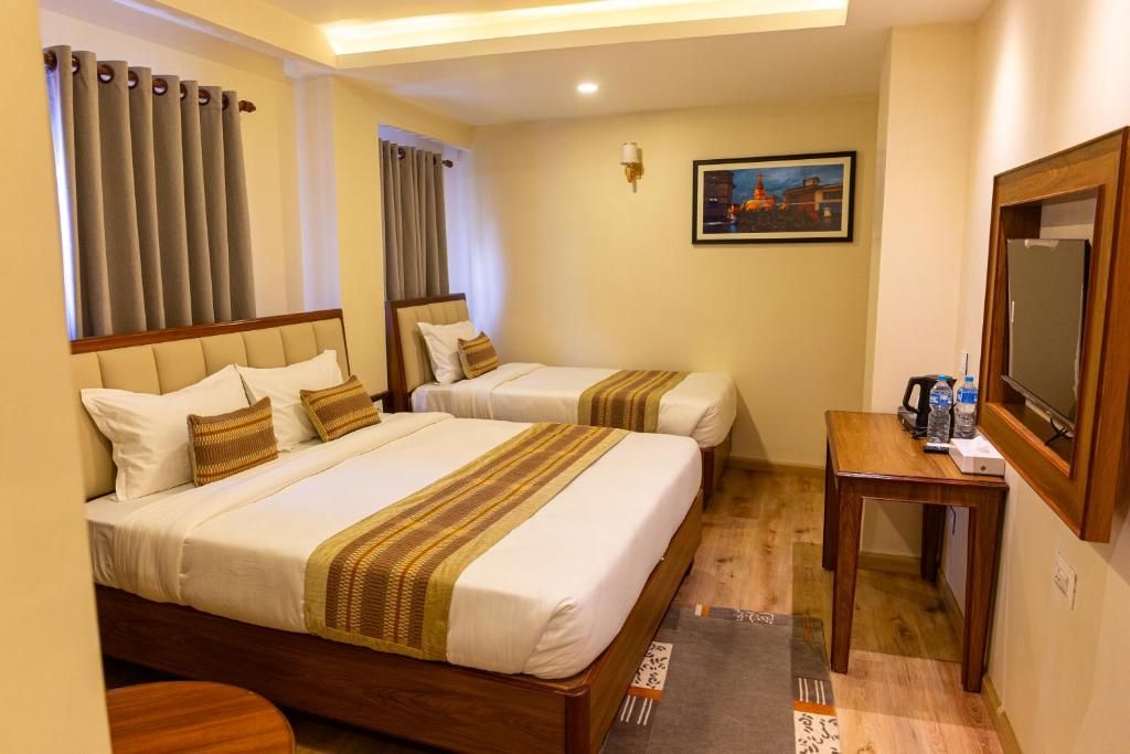 Habitación de hotel con dos camas, un escritorio, un televisor y un cuadro en la pared.