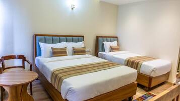Habitación de hotel con dos camas, una silla de madera y una mesita.