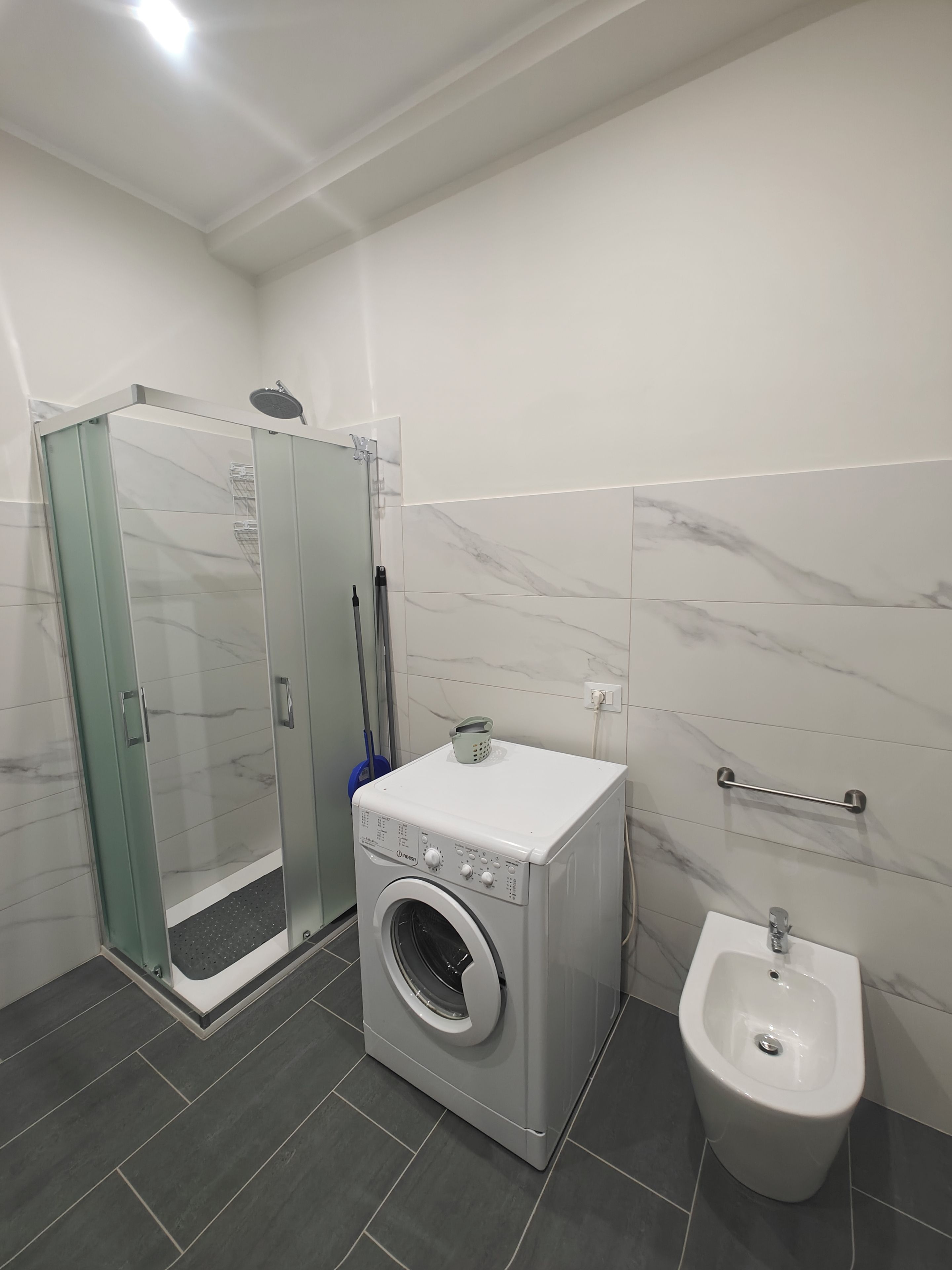 A modern bathroom with a glass-enclosed shower, a front-loading washing machine, and a pedestal bidet.