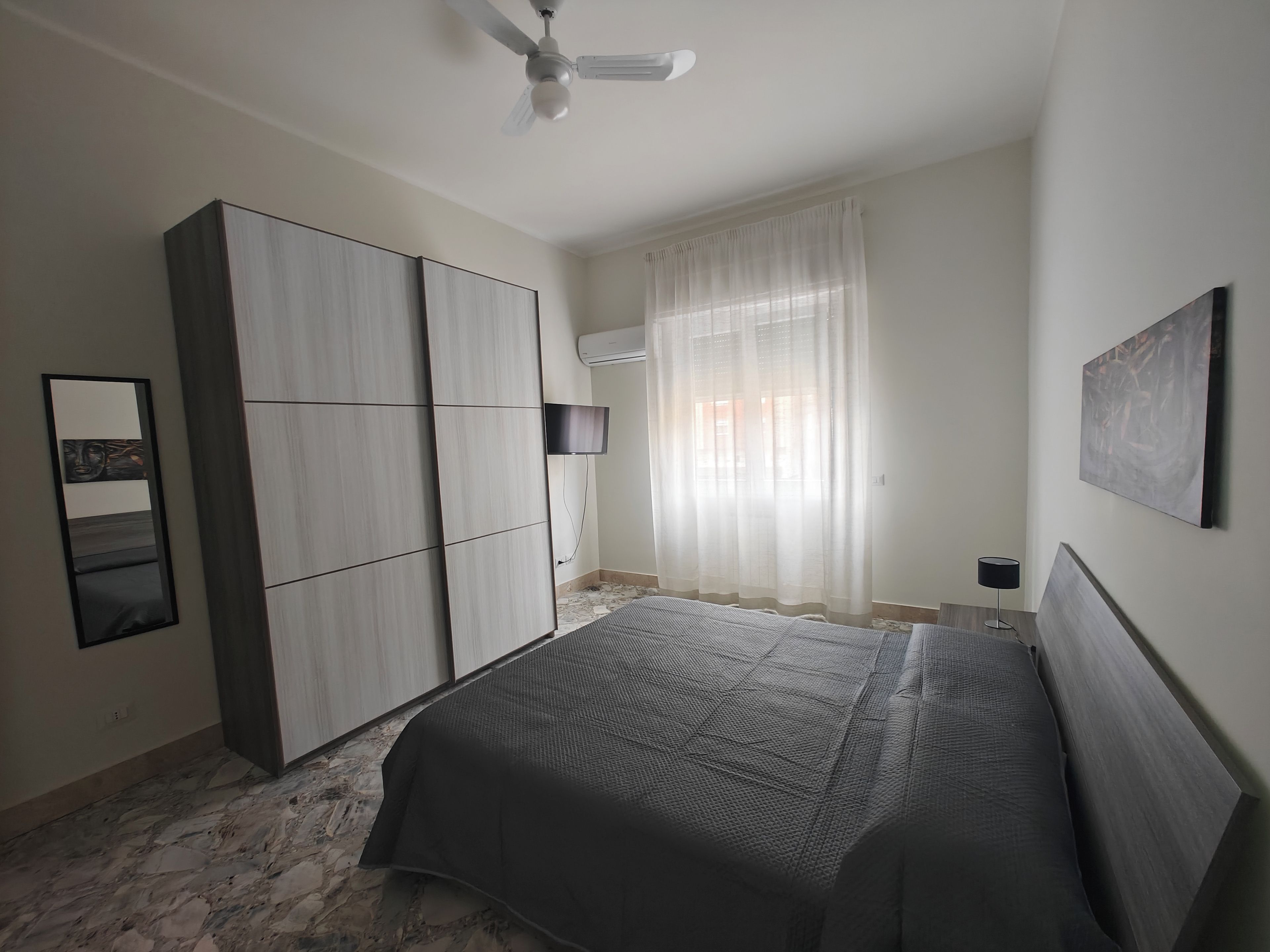 Une chambre à coucher comprenant un lit, une armoire, un ventilateur de plafond et des œuvres d’art accrochées au mur.
