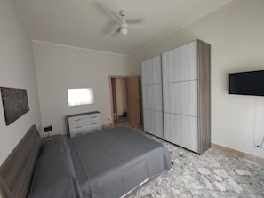Un dormitorio con una cama, un armario, un televisor y un ventilador de techo.