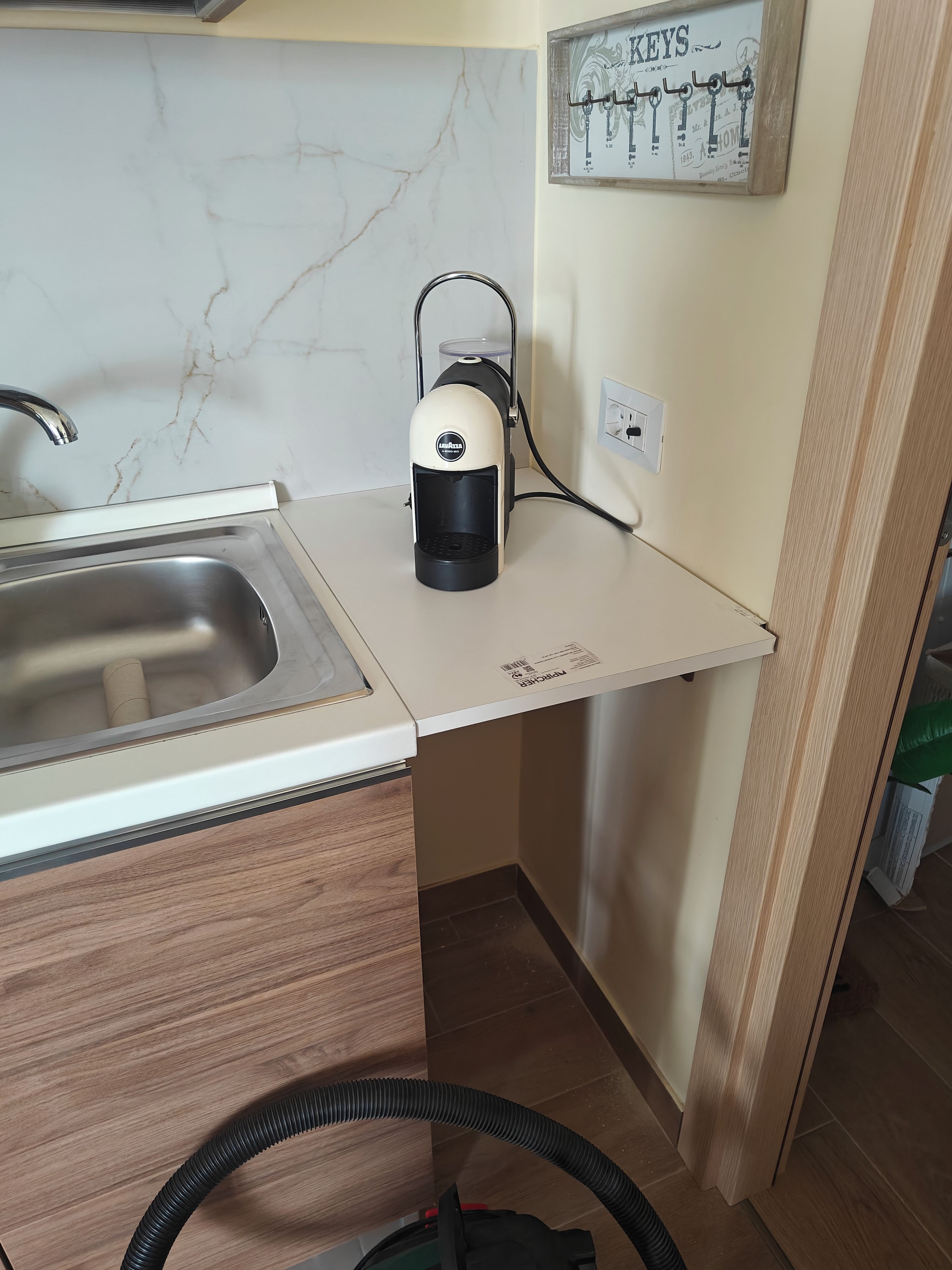 Une cuisine équipée d’un évier en acier inoxydable, d’une machine à café et d’une prise électrique murale.