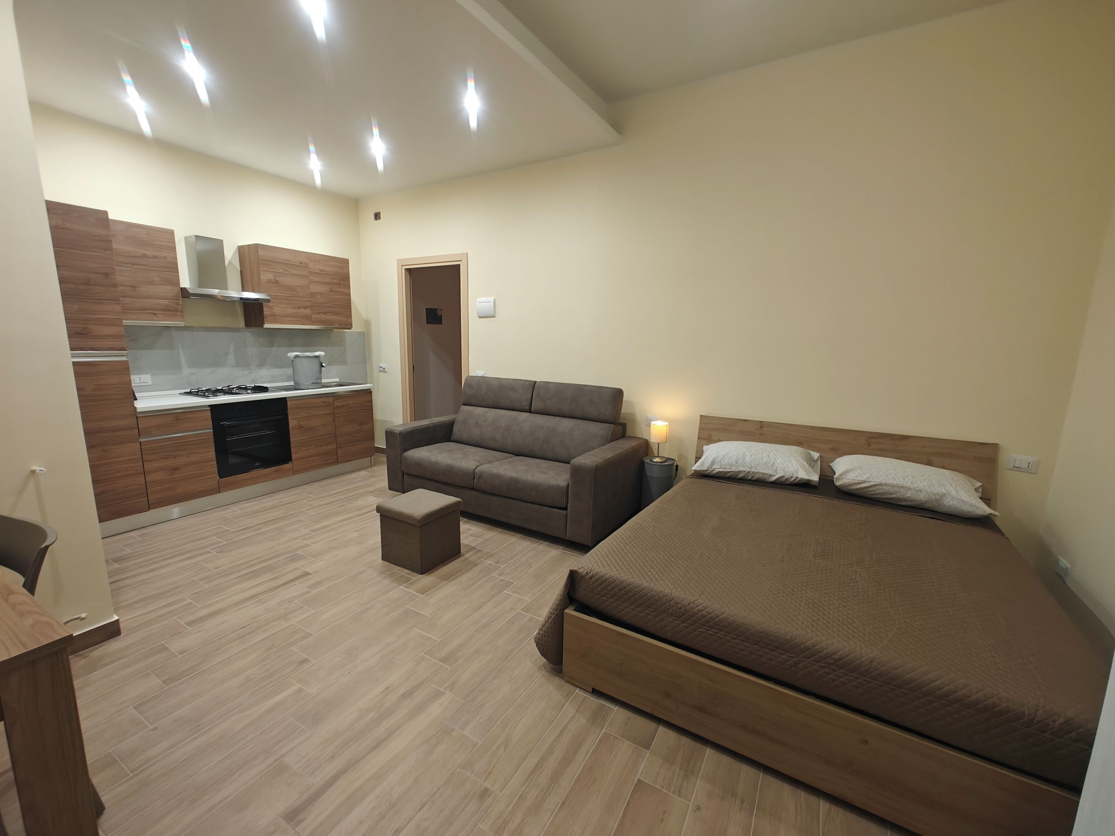 Una habitación funcional con kitchenette, cama, sofá y una pequeña mesa.