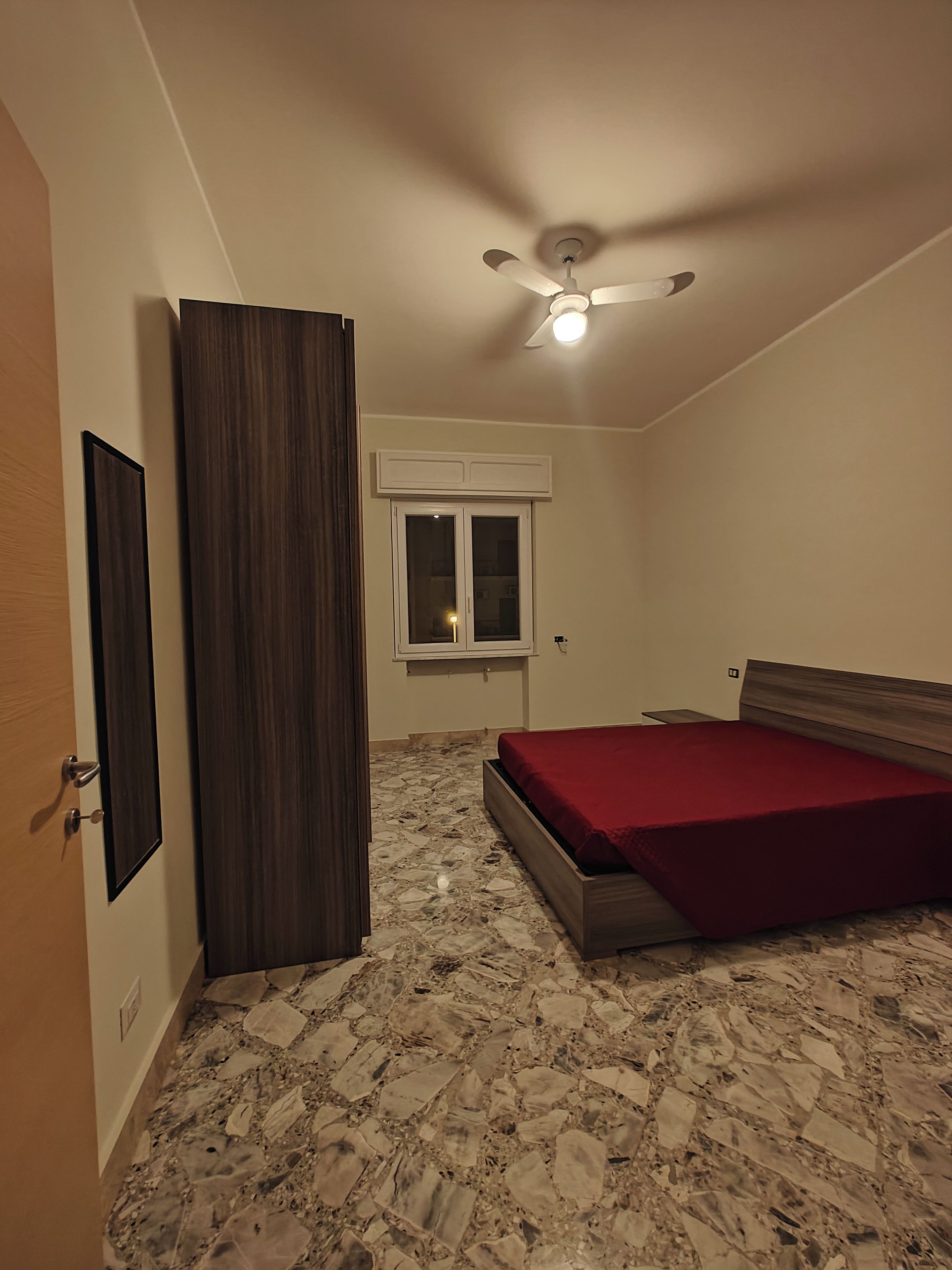 A bedroom with a bed, a wardrobe, a ceiling fan, and a window.