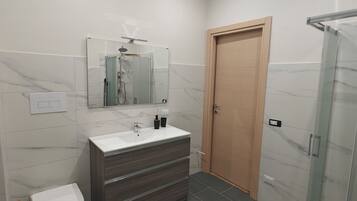 Une salle de bain moderne avec un lavabo blanc, un meuble-lavabo en bois foncé, une cabine de douche en verre et une porte en bois.