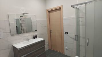 A modern bathroom with a white sink, dark wooden vanity, a glass shower enclosure, and a wooden door.