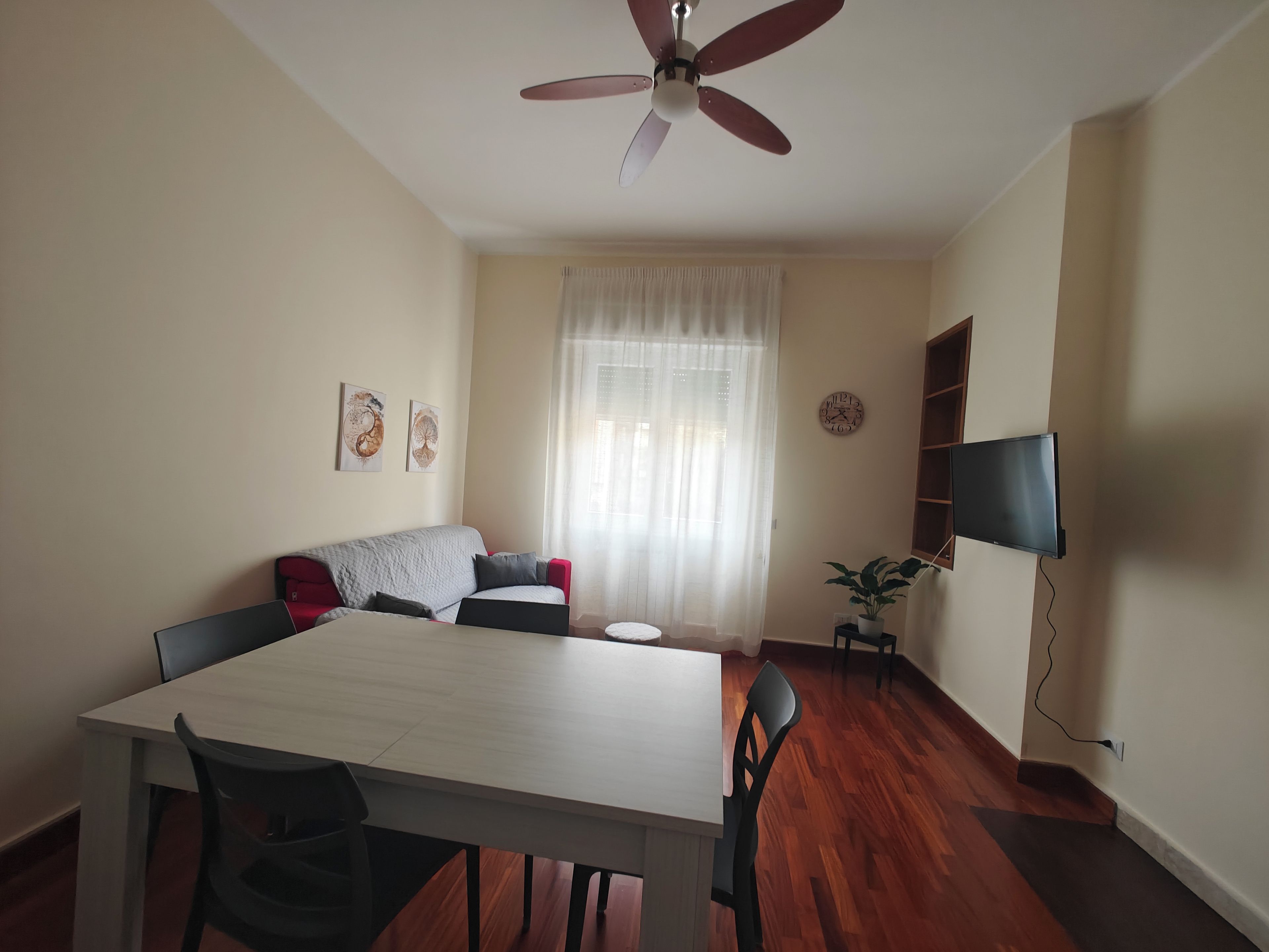 A dining area with a table, chairs, a ceiling fan, a sofa, a television, and a plant.