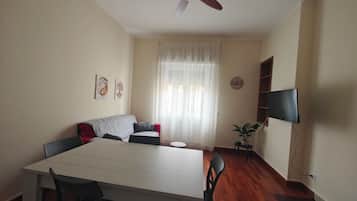 A dining area with a table, chairs, a ceiling fan, a sofa, a television, and a plant.