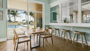 A dining area with a pool view, a bar with stools, and a large window. - Ocean View Escape: 2BR Villa at Marriott’s Oceana Palms (Riviera Beach)