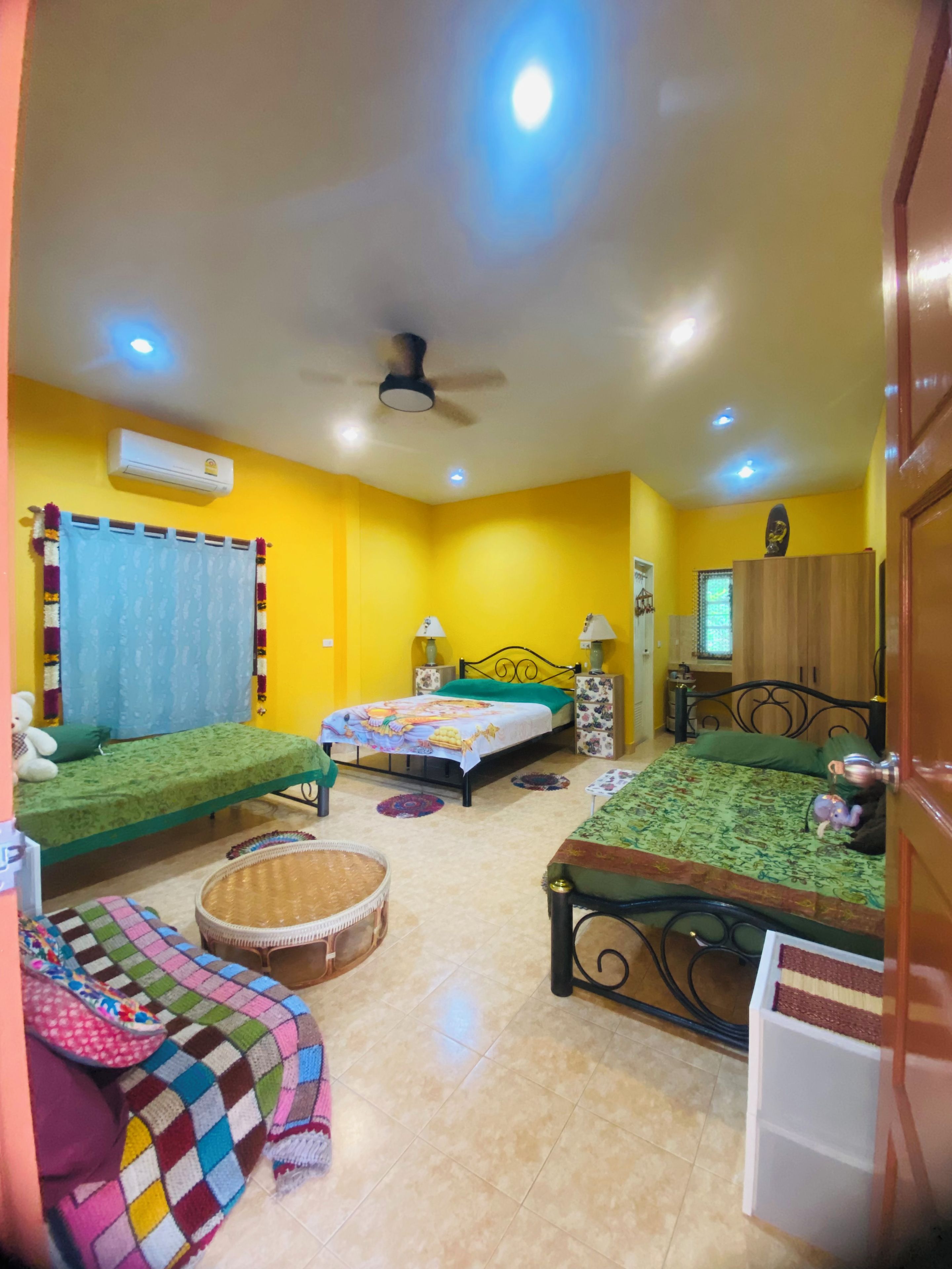 A room with two beds, a ceiling fan, an air conditioning unit, and a window with curtains.