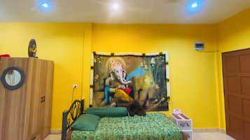 A room with a bed, a small table, a chair, a ceiling fan, and a wall tapestry.