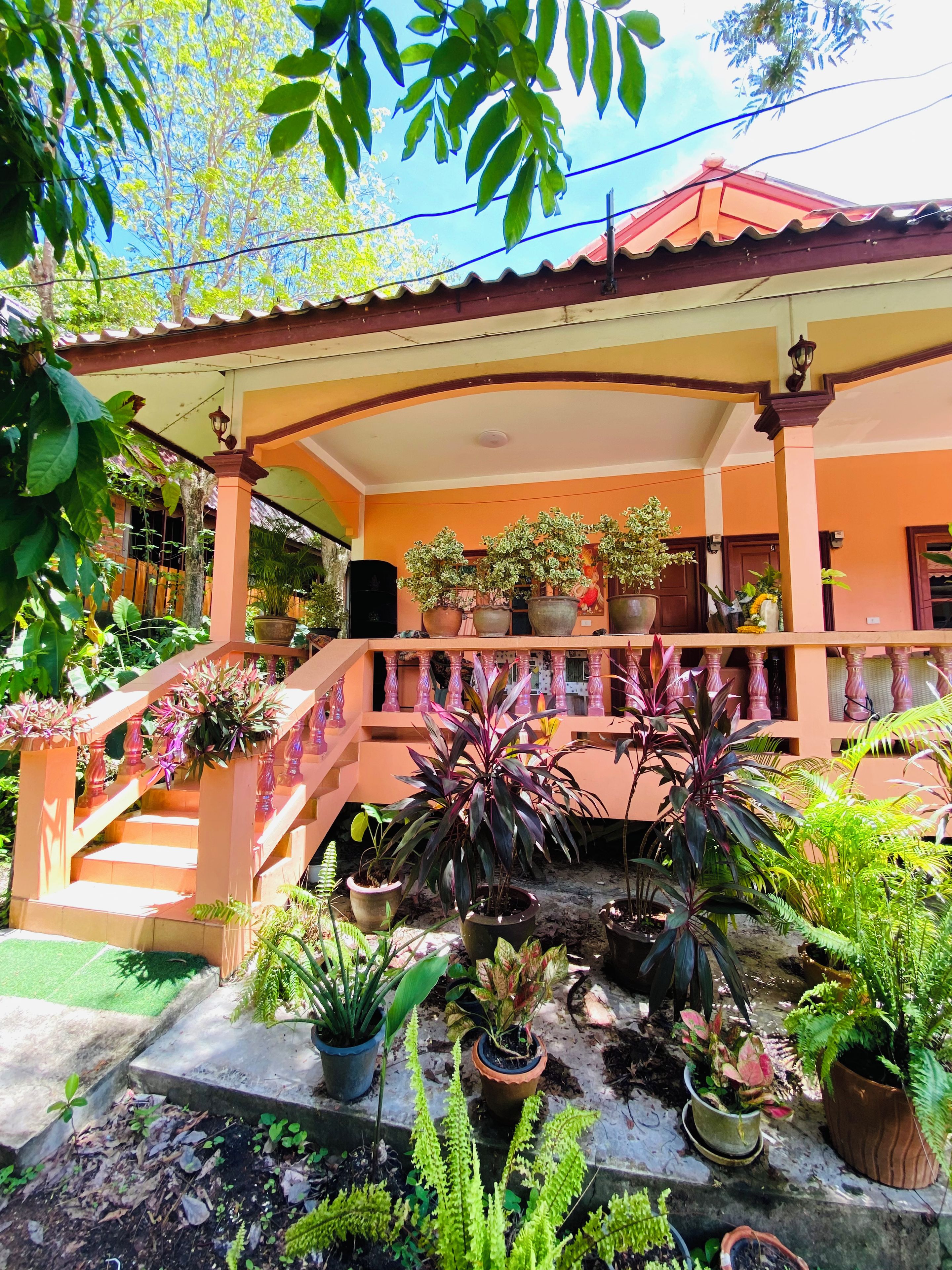 A covered outdoor area with a staircase, potted plants, and a building with orange walls and a red roof.