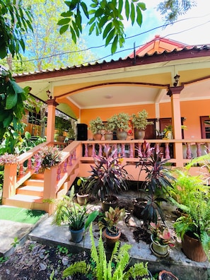Un espacio al aire libre cubierto con una escalera, plantas en macetas y un edificio con paredes anaranjadas y techo rojo.