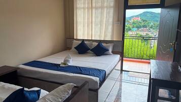 Una habitación de hotel con cama, escritorio y balcón con vistas a un paisaje verde.