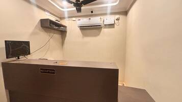A reception area with a reception desk, ceiling fan, air conditioning units, and a wall-mounted television.