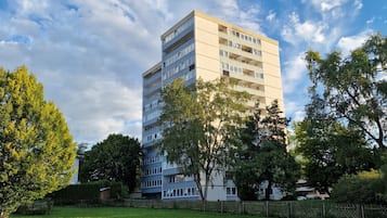 Ein mehrgeschossiges Gebäude mit flachem Dach, umgeben von einer Rasenfläche und Bäumen.