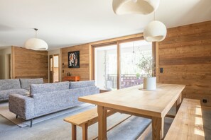 A modern living room with a wooden floor, a large sofa, a wooden dining table, and pendant lights. - Marion's Chalet, surrounded by nature, 15 minutes from Chamonix (Vallorcine)