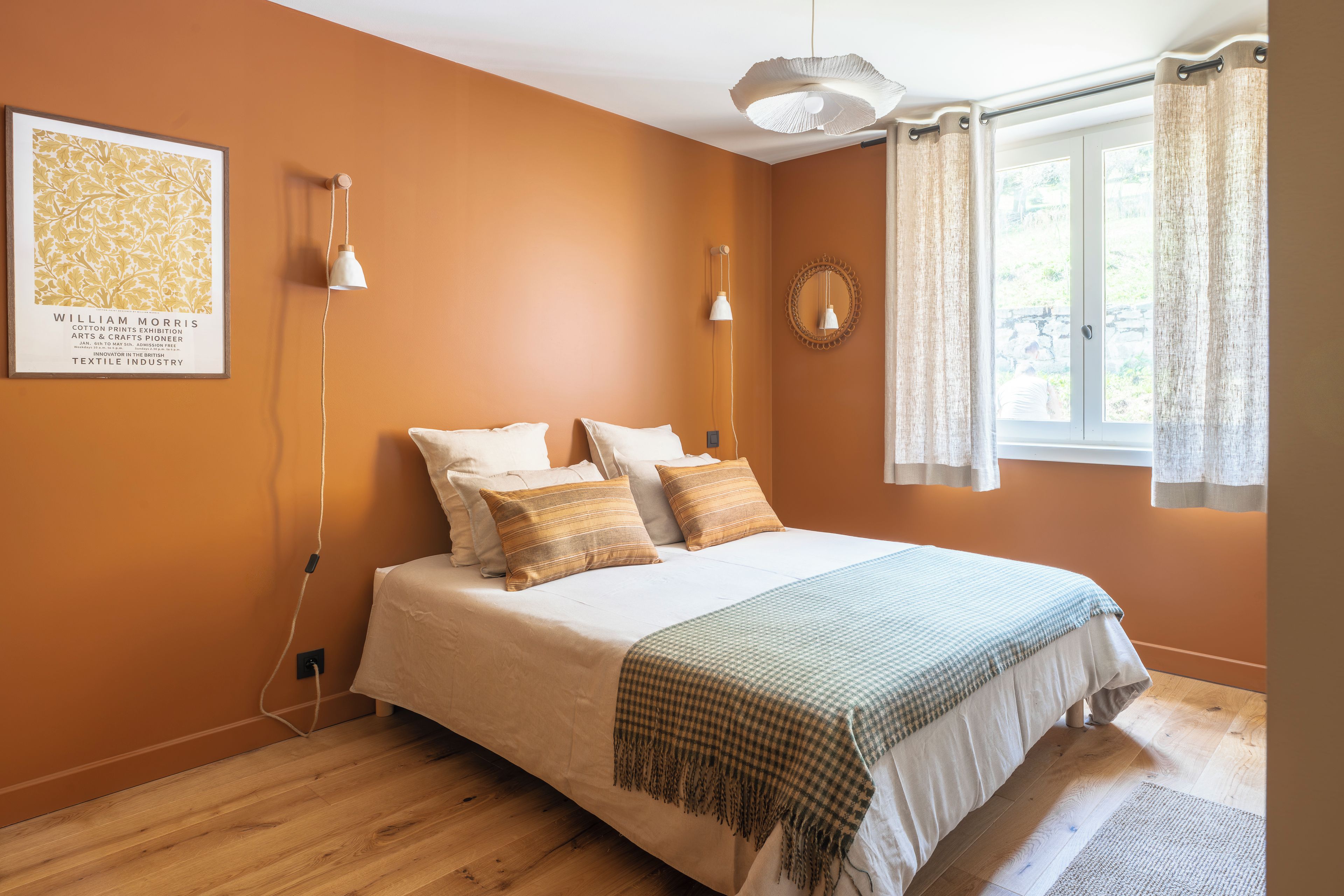 A bedroom with a bed, two wall-mounted lamps, a framed picture, and a window with curtains.