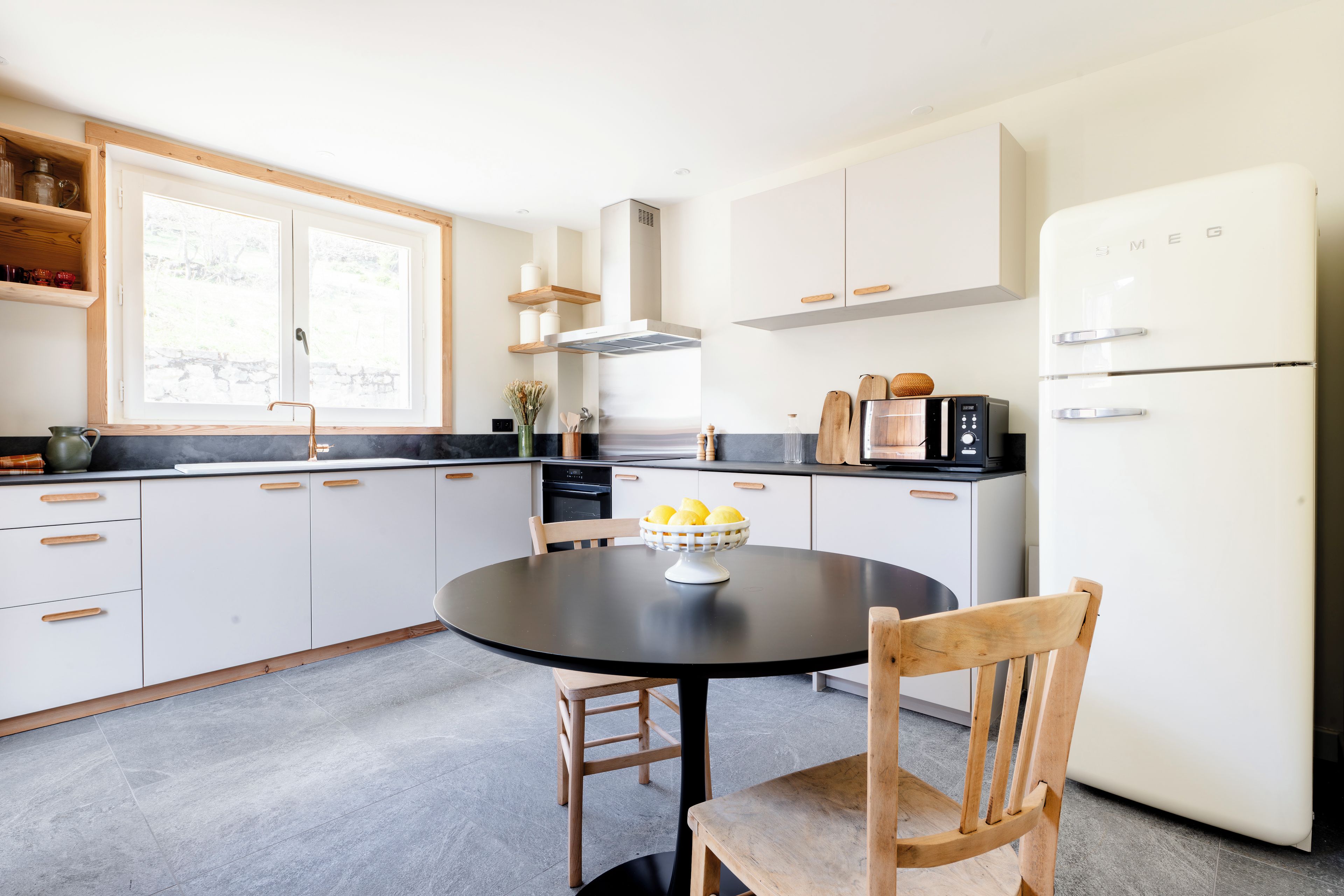 A modern kitchen with white cabinets, a black countertop, a round dining table with chairs, and a refrigerator.