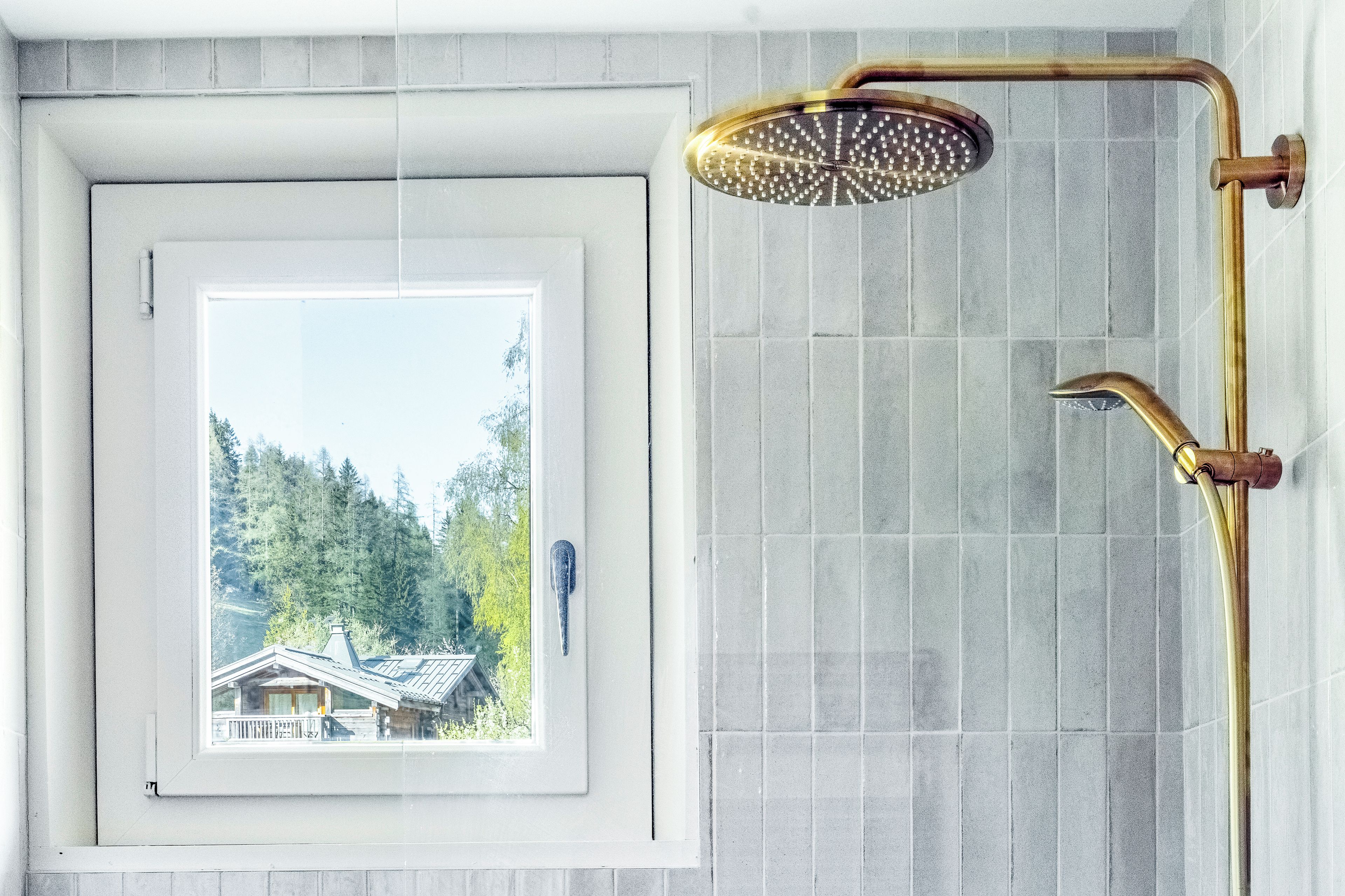 A bathroom with a shower, a window with a view of a house, and a tiled wall.