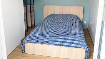 A bedroom with a bed, a wooden headboard, two wall-mounted lamps, a framed picture, a woven rug, and a ladder against the wall.