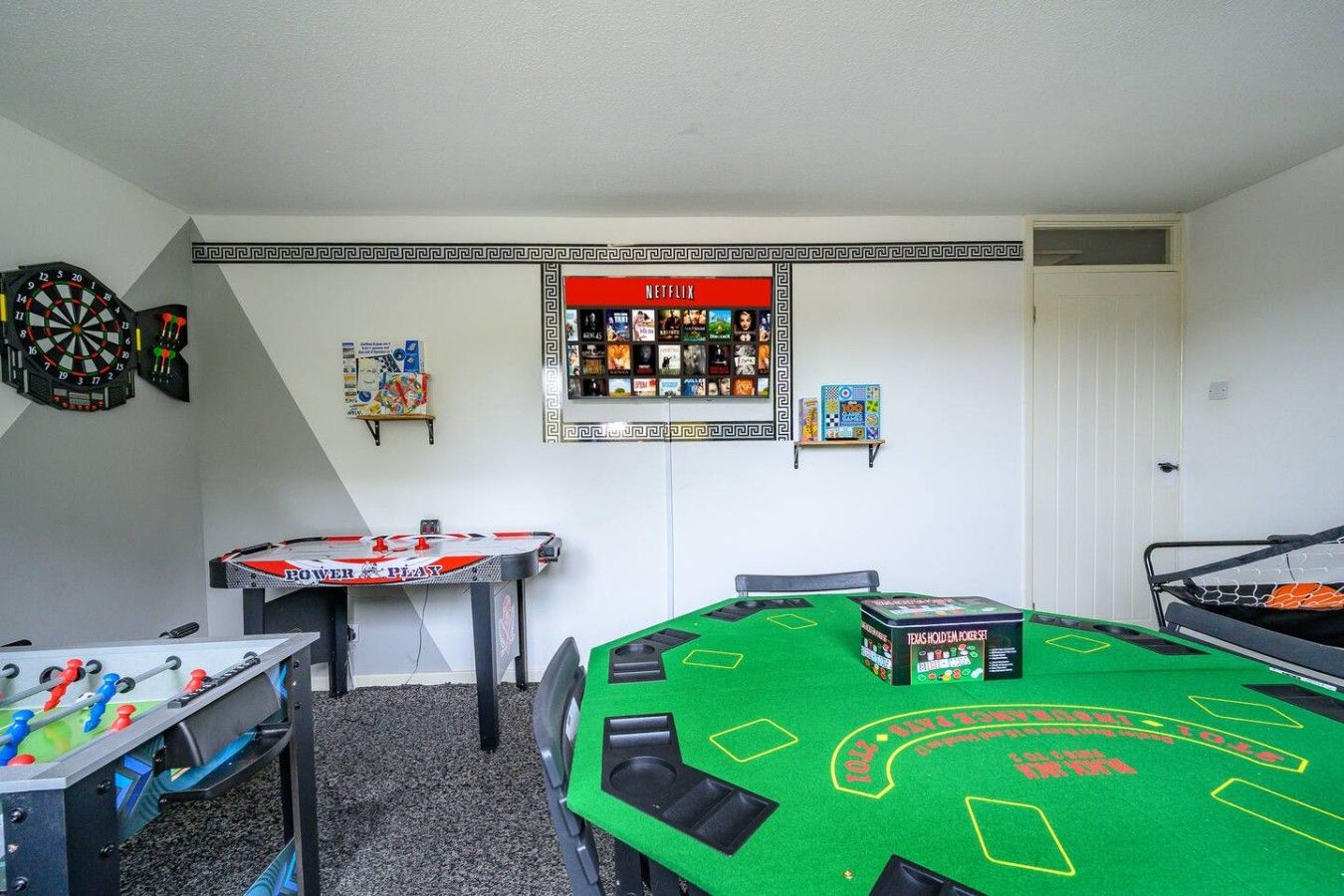 A room with a dartboard, a table with a board game, and a wall with a Netflix sign.