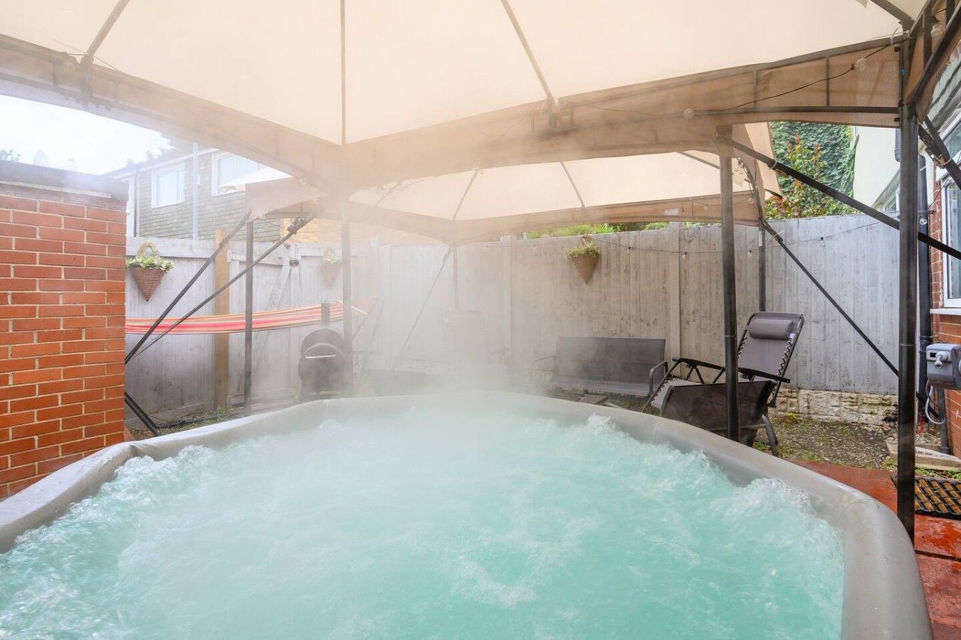 A hot tub in a covered outdoor area with a brick wall and a wooden fence in the background.