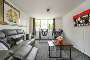Un salon moderne avec un canapé en cuir, une table basse, un hamac et un écran Netflix fixé au mur.
