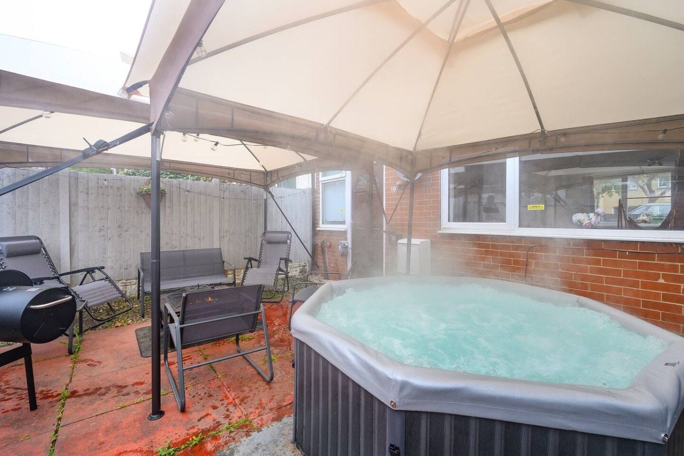 A hot tub under a tent, surrounded by outdoor furniture and a brick wall.