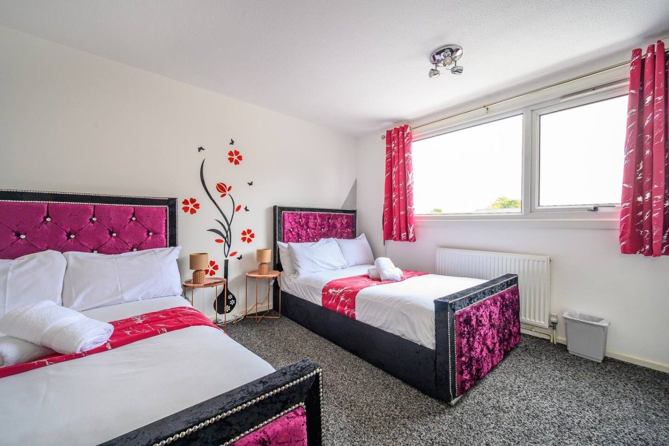 A hotel room with two beds, a radiator, a window with curtains, and a wall decoration.