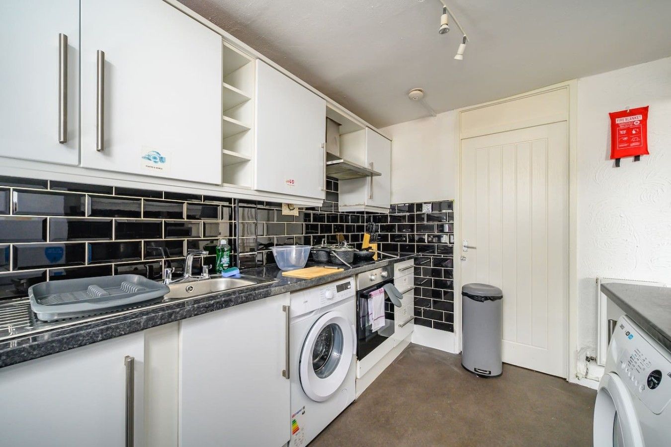A compact kitchen with a washing machine, a sink, and a trash bin.