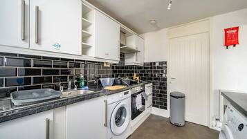 A compact kitchen with a washing machine, a sink, and a trash bin.