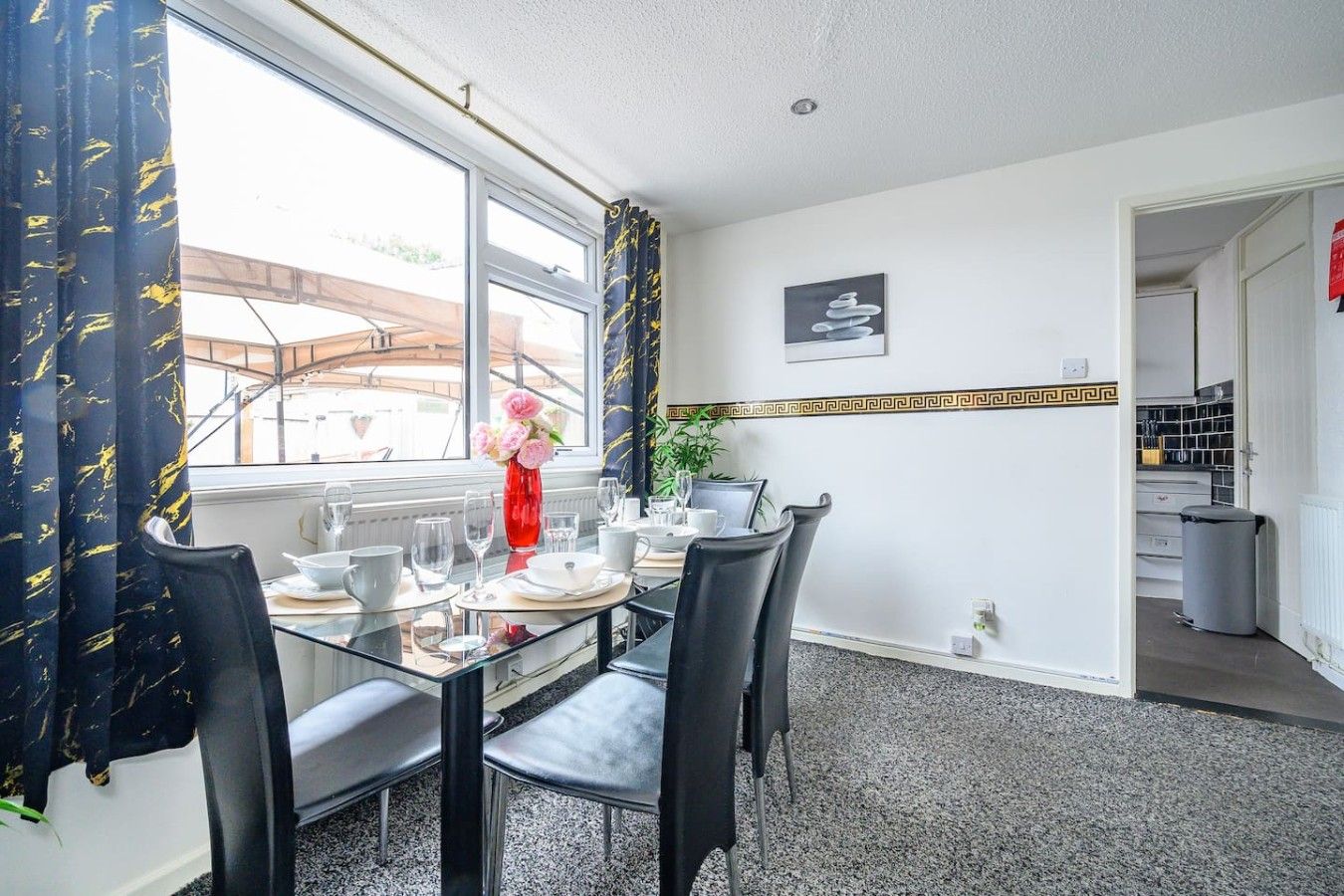 A dining area with a glass table, black chairs, and a vase of flowers.