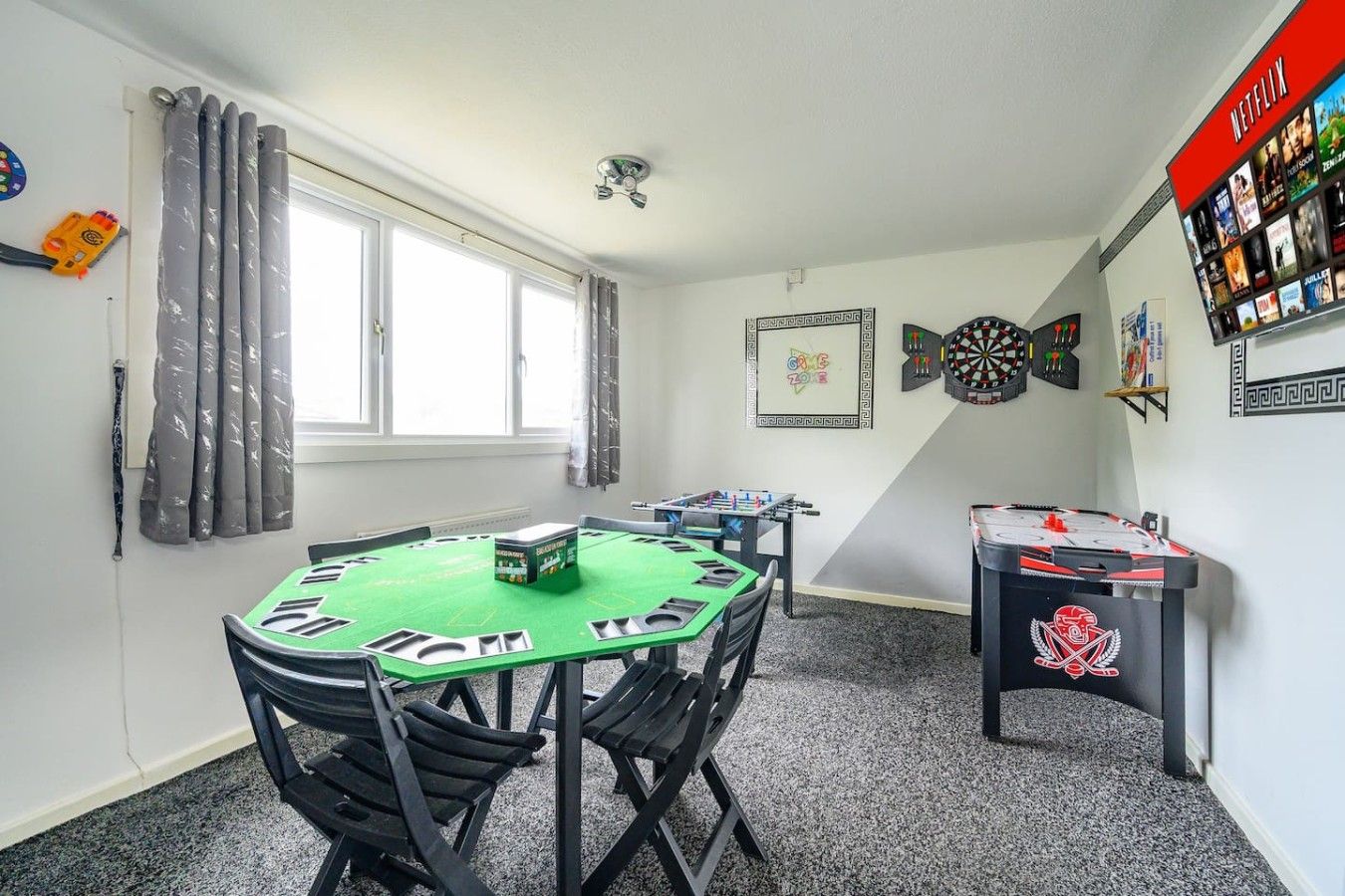 A room with a green table, chairs, a dartboard, a foosball table, and a Netflix sign.