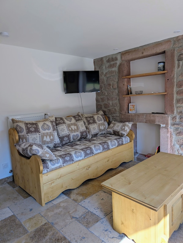 Ein Wohnzimmer mit einer Holzsofa, einem an der Wand montierten Fernseher und einem Couchtisch aus Holz.