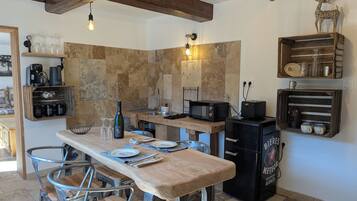 Une cuisine avec une table en bois, des chaises en métal, un réfrigérateur noir et un pare-feu en pierre.