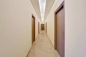 Un pasillo largo y estrecho con puertas a ambos lados, que da acceso a habitaciones. El suelo está cubierto de baldosas y las paredes son de un color claro.