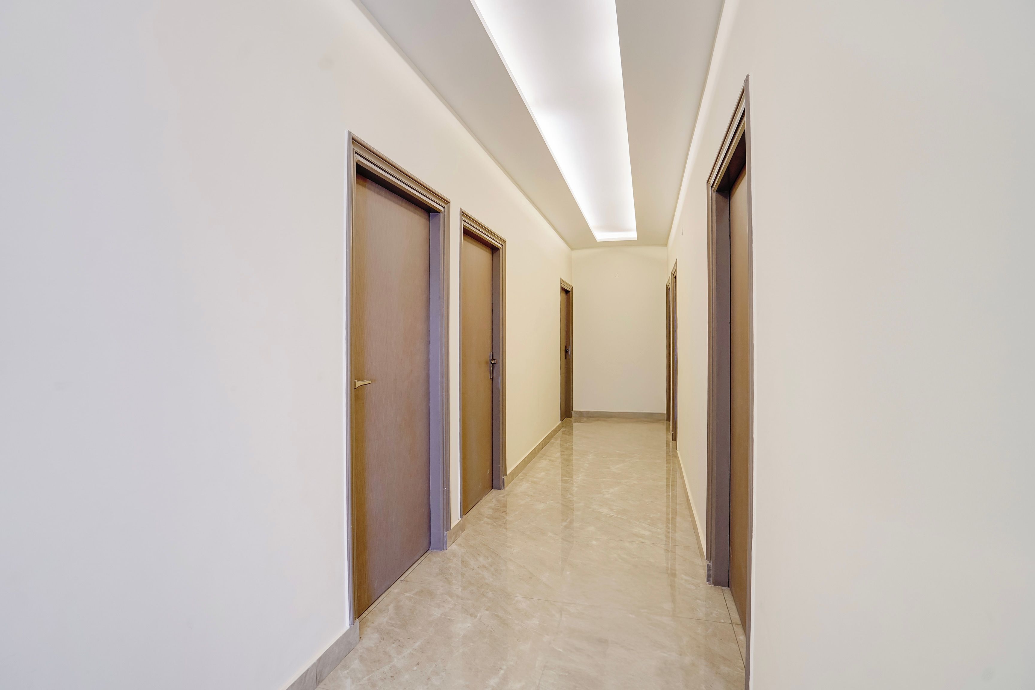 A corridor with doors on both sides, a tiled floor, and a ceiling with recessed lighting.