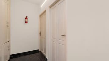 A hallway with white doors, a fire extinguisher mounted on the wall, and a black tiled floor.