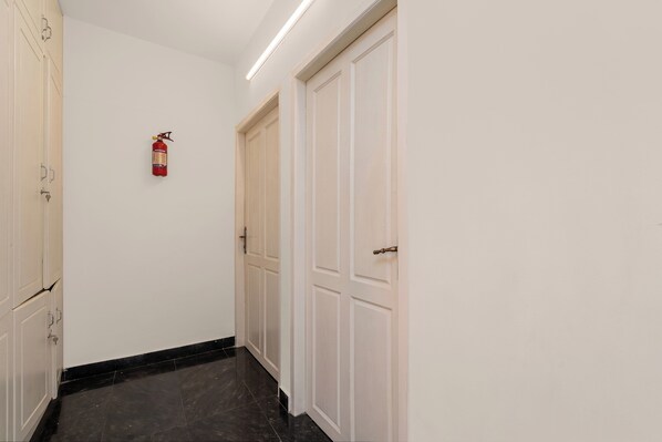 A hallway with white doors, a fire extinguisher mounted on the wall, and a black tiled floor.