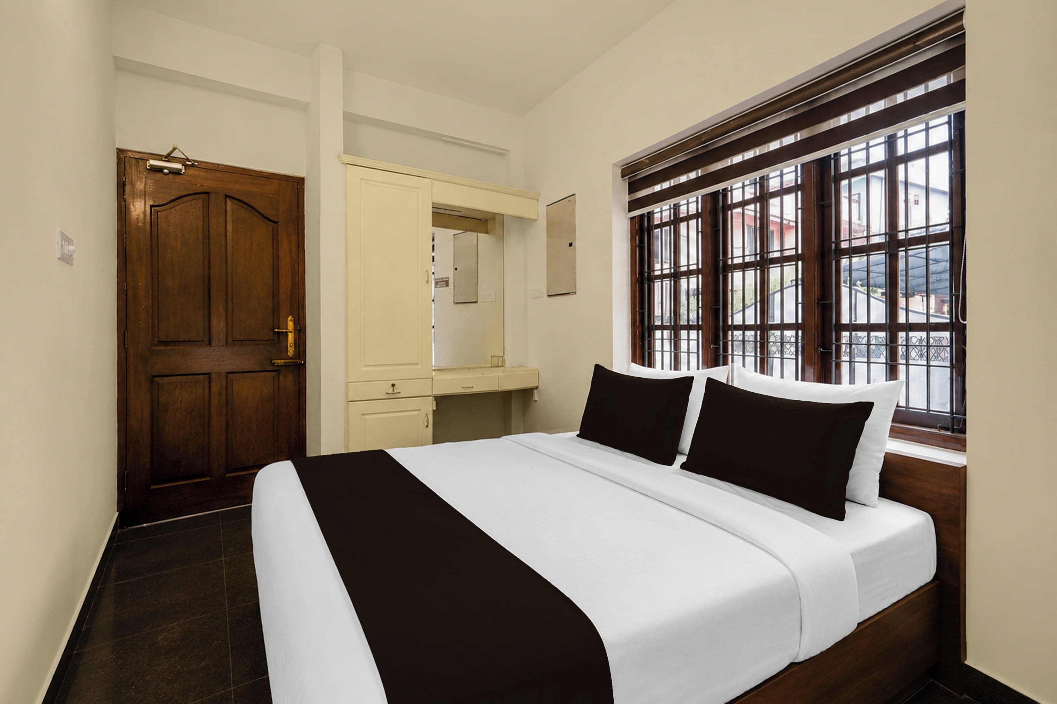Una habitación de hotel con una cama grande, una puerta de madera, una ventana con barrotes y un escritorio pequeño con espejo.