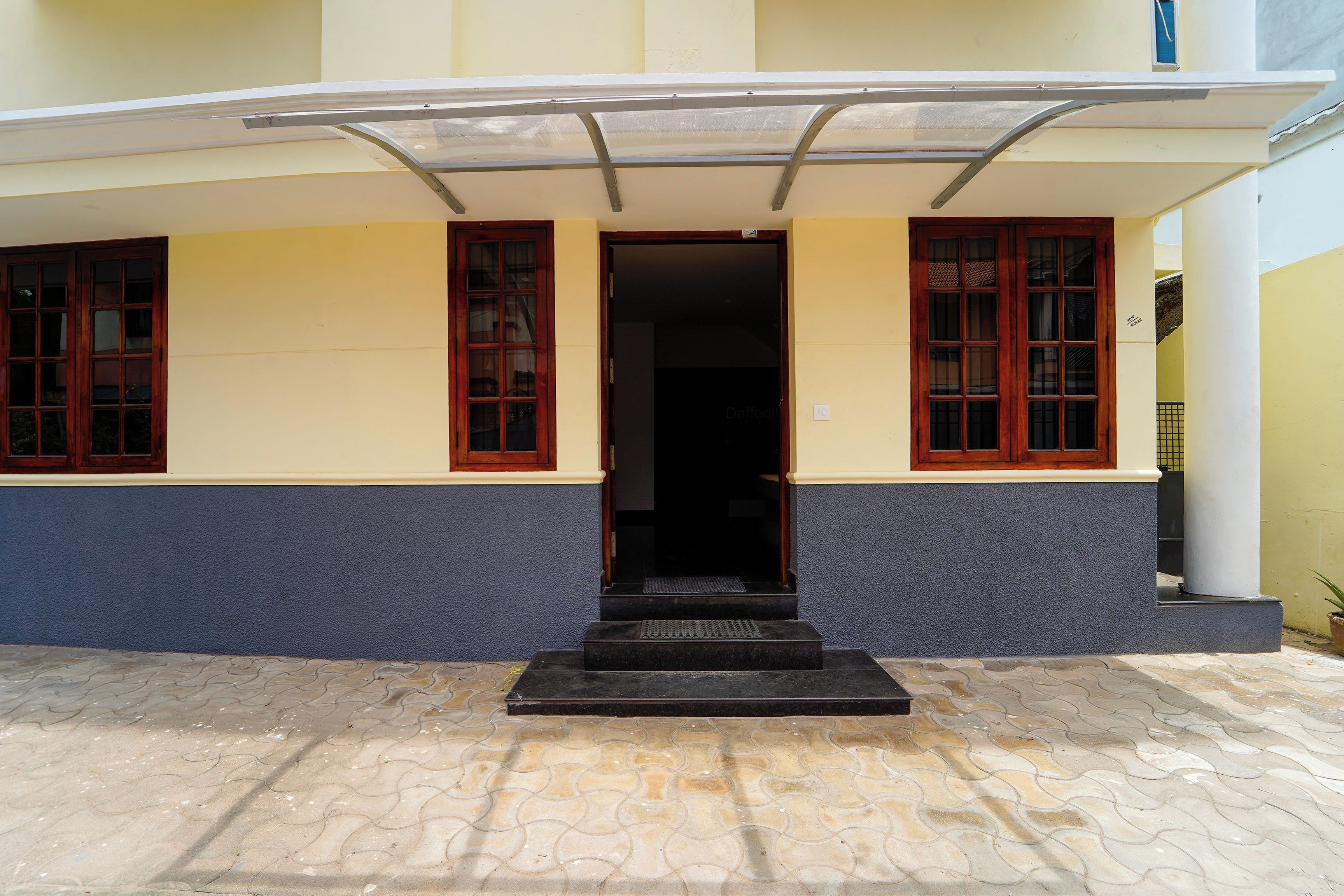 Entrada de um edifício com um conjunto de degraus que levam a uma porta, ladeada por duas janelas com molduras de madeira.