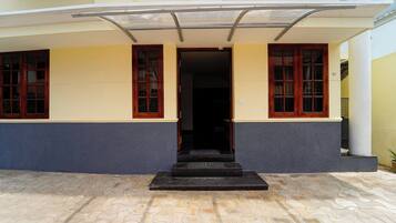 Entrada de um edifício com um conjunto de degraus que levam a uma porta, ladeada por duas janelas com molduras de madeira.
