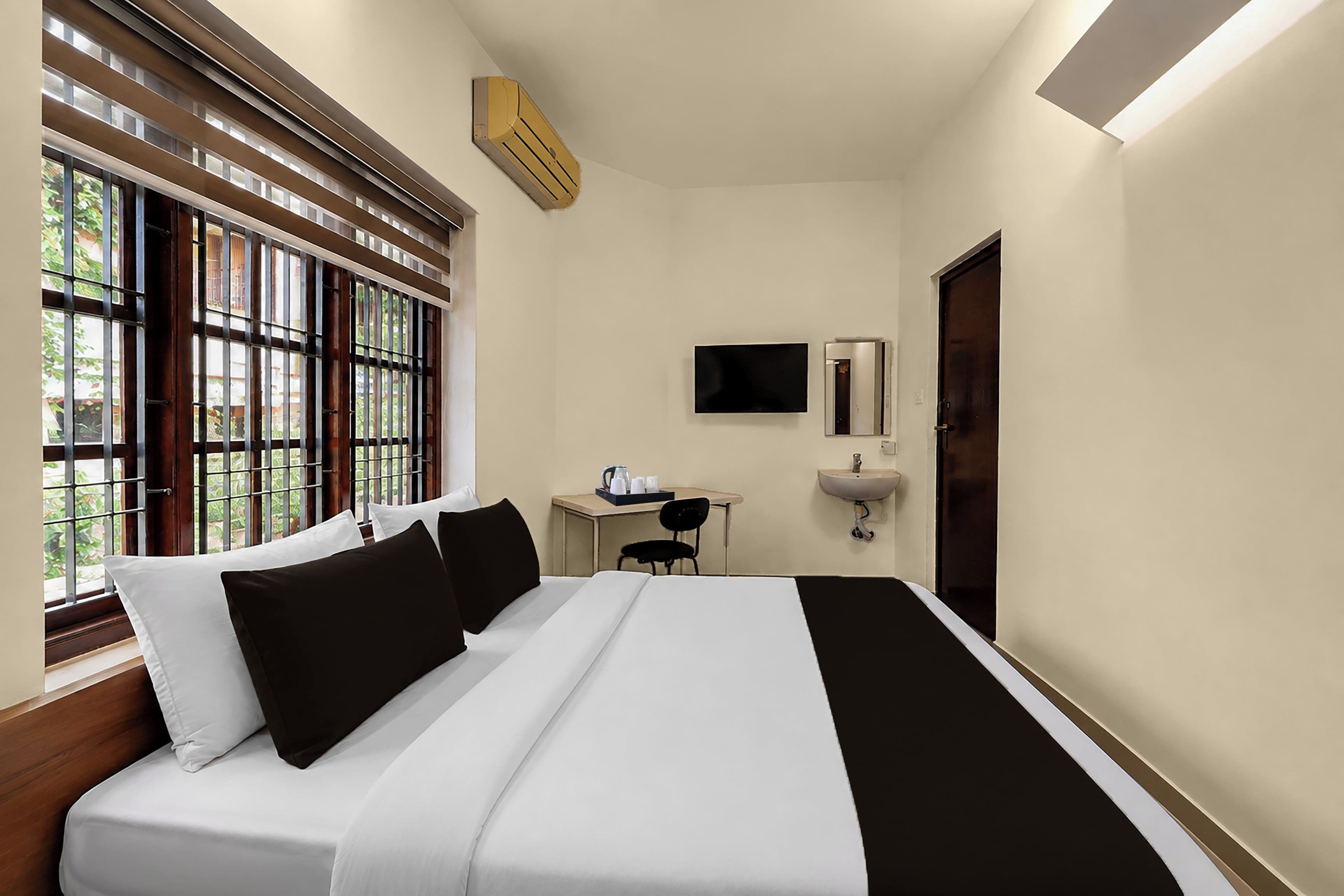 Habitación de hotel con cama, escritorio, silla, televisor y ventana con persianas.