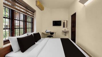 Habitación de hotel con cama, escritorio, silla, televisor y ventana con persianas.