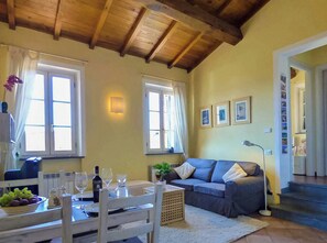 A cozy living room with a wooden ceiling, a dining table with wine glasses, a sofa, and a staircase leading to another room. - Lucca apartment with private furnished terrace (Lucca)